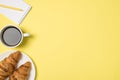 Top view photo of cup of coffee plate with two fresh croissants and yellow pencil on small notepad on isolated light yellow Royalty Free Stock Photo