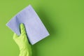 Top view photo of hand in green rubber glove holding lilac napkin on isolated green background with copyspace Royalty Free Stock Photo