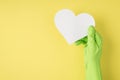 Top view photo of hand in green rubber glove holding white paper heart on isolated yellow background with blank space Royalty Free Stock Photo