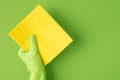 Top view photo of hand in green rubber glove holding yellow rag on isolated green background with blank space Royalty Free Stock Photo