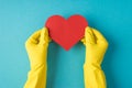 Top view photo of hands in yellow rubber gloves holding red paper heart on isolated pastel blue background with blank space Royalty Free Stock Photo