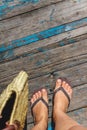Top view, photo of legs in beach flip-flops and with a straw bag in hand on a wooden old floor. Photos on vacation, beach, summer Royalty Free Stock Photo