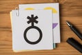 Top view photo of non-binary flag and black genderqueer symbol on stickers and pen on wooden table background