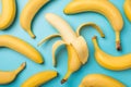 Top view photo of one peeled banana in the middle and scattered unpeeled bananas on isolated pastel blue background Royalty Free Stock Photo