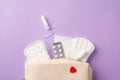 Top view photo of open medicine bag with hygienic pads tampon and plate of pills on isolated pastel purple background