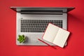 Top view photo of open red notebook pencil and flowerpot on open grey laptop on isolated red background with blank space