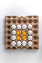 Top view photo of raw chicken eggs on recyclable cardboard tray, four broken with yolk on the top, paper packaging pattern with