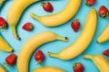 Top view photo of ripe yellow bananas and scattered strawberries with leaves on isolated light blue background Royalty Free Stock Photo