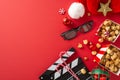 Top-view photo showcasing a movie clapper, 3D glasses, popcorn, Santa\'s hat, baubles, star decor on a red background