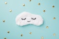 Top view photo of the soft cute white sleep mask in the middle of the pastel blue background with a lot of confetti in shape of
