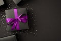 Top view photo of stylish black gift boxes with purple ribbon bow and sequins on black background with copyspace