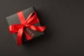 Top view photo of stylish giftbox in black packaging with vivid red satin ribbon bow and tag on isolated black background with Royalty Free Stock Photo