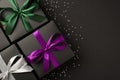 Top view photo of three stylish black gift boxes with purple green and white satin ribbon bows and sequins on  black Royalty Free Stock Photo