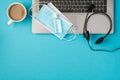 Top view photo of two medical facemasks and transparent sanitizer bottle on laptop headphones and cup of drink on isolated pastel