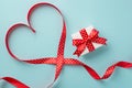 Top view photo of valentine`s day decorations red ribbon heart and white giftbox with red bow on isolated pastel blue background Royalty Free Stock Photo