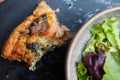 Top view of a piece of spinach and salmon quiche and salad on the side on a board