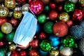 Top view of a pile of dark and colorful Christmas balls with a surgical face mask for holiday celebration during covid-19 pandemic Royalty Free Stock Photo