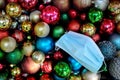 Top view of a pile of dark and colorful Christmas balls with a surgical face mask for holiday celebration during covid-19 pandemic Royalty Free Stock Photo