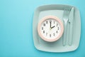 Top view of pink alarm clock with plate, fork and knife on blue background - concept and idea Royalty Free Stock Photo