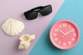 Top view pink alarm clock and sunglasses and shells on a colorful background, like a time at sea Royalty Free Stock Photo