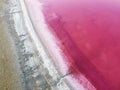 Top view of a pink lake and the shore is covered with a rough layer of salt