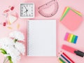 Top view of pink office desktop with notebook in cage, flowers,