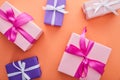 Top view of pink and purple gift boxes with ribbons and bows on orange background.