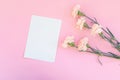 Top view of a pink table with a layout of empty notebooks and a bouquet of carnations. Place for text