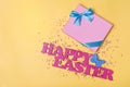 Pink text of happy easter and gift box with blue satin bow and bright colorful sugar sprinkles Royalty Free Stock Photo