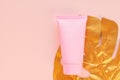 Top view of a pink tube of cream mockup with a golden monstera leaf on a pink background. Unbranded cosmetics package