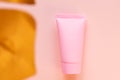 Top view of a pink tube of cream mockup with a golden monstera leaf on a pink background. Unbranded cosmetics package