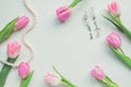 Top view of pink tulips, earrings and string of pearls on white background with copy space