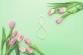 Top view of pink tulips and figure eight made of string of pearls on light green background with copy space