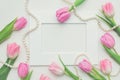 Top view of pink tulips, photo frame and string of pearls on white background with copy space