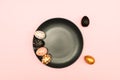 Top view of pink, white and golden decorated eeaster eggs on black plate on pink background. Trendy holiday backdrop