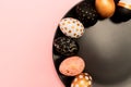 Top view of pink, white and golden decorated eeaster eggs on black plate on pink background. Trendy holiday backdrop