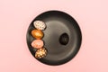 Top view of pink, white and golden decorated eeaster eggs on black plate on pink background. Trendy holiday backdrop