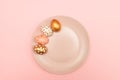 Top view of pink, white and golden decorated eeaster eggs on pink plate on pink background. Trendy holiday backdrop