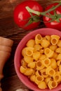 top view of pipe-rigate pasta in bowl with tomatoes and salt on wooden background