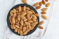 Top view plate with almonds in endocarp, bowl with drupe in shell on a white wooden cutting board. White background, overhead,