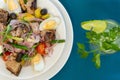 Top view of a plate of Salade nicoise and glass of mojito on blue table