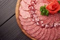 Top view of plate of sliced sausage decorated with aromatic herbs. Sausage on wooden catering platter, flat lay of meat