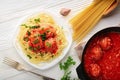 Top view of plate of spaghetti with meatballs in tomato sauce and pan with meatballs on white wooden background Royalty Free Stock Photo