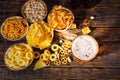 Top view of plates with snacks near glass of beer, wheat, scattered nuts and pretzels on dark wooden desk Royalty Free Stock Photo