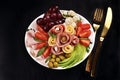 Top view of a platter with assortment of sliced ham and cheese with vegetables and grape on black background Royalty Free Stock Photo