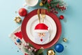 Top view of cutlery pocket, elegant plates, napkin, cozy mug, festive baubles, frost-kissed fir twigs, berries, blue backdrop