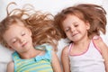 Top view of pleased attractive small girls or sisters smile together, sleep in bed, lie closely to each other, see pleasant dreams