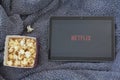 Top view of popcorn box, tablet with netflix logo and warm blanket