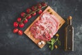 Top view of pork steaks chops on a wooden board, next to a sprig of basil, cherry tomatoes on a branch and a bottle of olive oil. Royalty Free Stock Photo