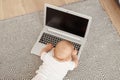 Top view portrait of cute baby wearing white t shirt lying on floor on carpet and using laptop, small kid touching pc computer Royalty Free Stock Photo